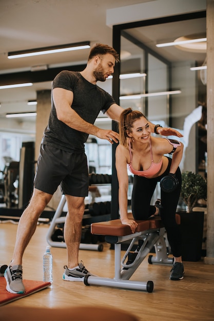 Mujer atractiva y un entrenador personal con pesas en el gimnasio