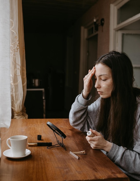 Foto mujer atractiva con el espejo haciendo maquillaje en casa con cosméticos y café