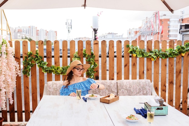 Mujer atractiva está almorzando, cenando en la terraza del café al aire libre, mirando sus relojes.