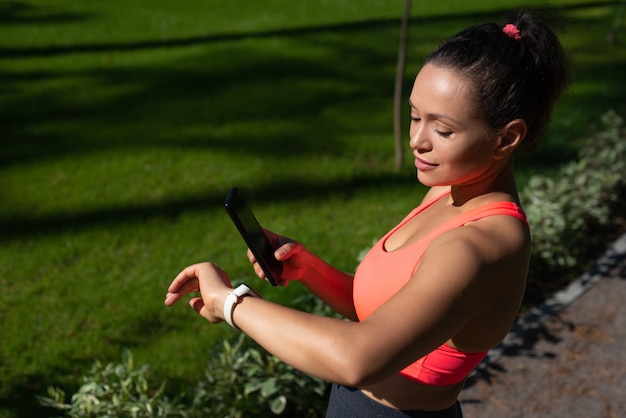 Mujer atractiva en forma que mira la pulsera de fitness y examina cómo se han perdido las calorías durante la carrera