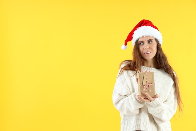 Mujer atractiva con gorro de Papá Noel tiene caja de regalo sobre fondo amarillo