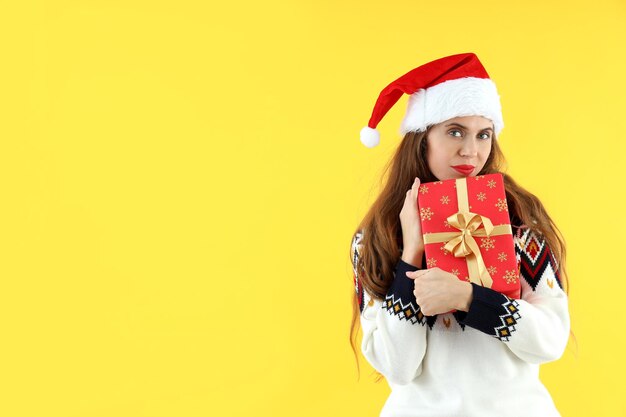 Mujer atractiva con gorro de Papá Noel tiene caja de regalo sobre fondo amarillo