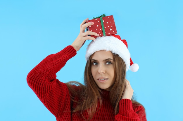 Mujer atractiva con gorro de Papá Noel tiene caja de regalo sobre fondo azul.