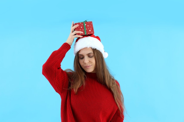 Mujer atractiva con gorro de Papá Noel tiene caja de regalo sobre fondo azul.