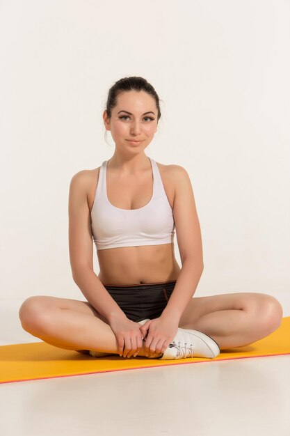 Foto mujer atractiva haciendo ejercicios de cuerpo en forma morena en estera de yoga