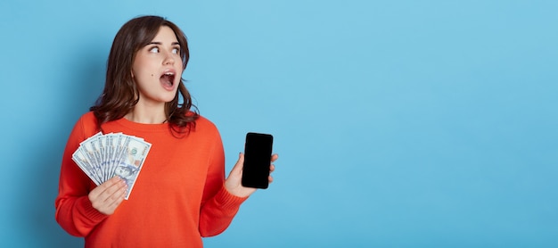 Foto mujer atractiva con increíble servicio de pago móvil, mujer sorprendida sosteniendo teléfono celular