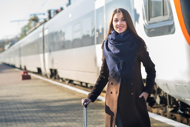 Mujer atractiva joven en abrigo con una maleta esperando en la estación de tren