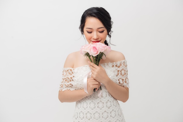 Mujer atractiva joven asiática feliz que sostiene el ramo de flores y que lleva el fondo blanco