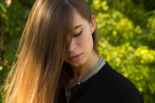 Mujer atractiva joven en blusa negra con collar de plata tocando su cabello largo