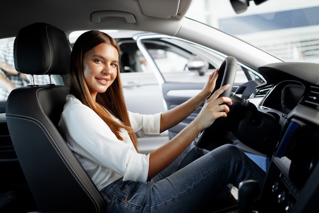 Mujer atractiva joven en busca de un coche nuevo en una sala de exposición de coches