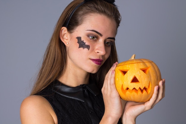 Mujer atractiva joven con calabazas en vestido negro sosteniendo una calabaza sobre fondo azul en estudio