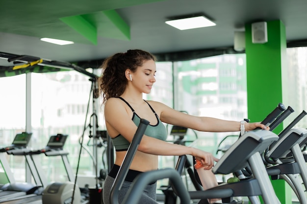 Mujer atractiva joven calentando en una máquina de ejercicio elíptica en el gimnasio. Fitness, concepto de estilo de vida saludable.