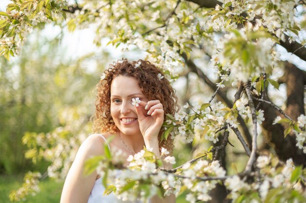 La mujer atractiva joven camina en el parque verde de la primavera que disfruta de la naturaleza floreciente. Mujer sonriente sana girando en el césped de primavera.