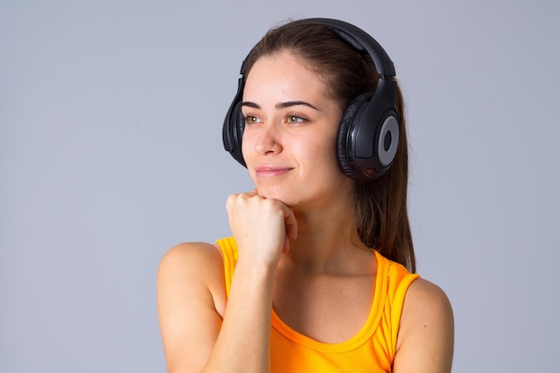 Mujer atractiva joven en camiseta escuchando la música en auriculares negros sobre fondo gris