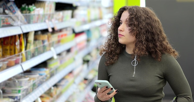 Mujer atractiva joven comprobando la lista de tareas pendientes en el teléfono inteligente en el supermercado Tienda en línea de hipermercados centros comerciales Mercado de alimentos para teléfonos inteligentes Comprador de alimentos para niñas