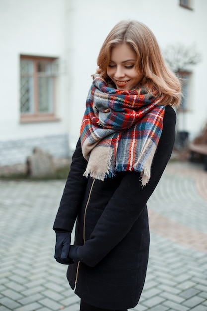 Mujer atractiva joven en un elegante abrigo de invierno en guantes negros en una bufanda de lana vintage de moda