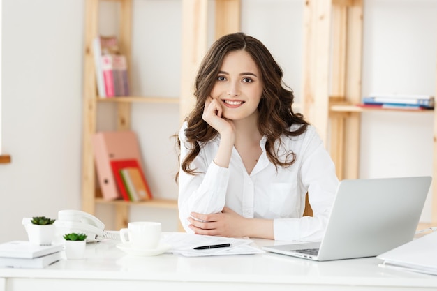 Mujer atractiva joven en un escritorio de oficina moderno trabajando con un portátil y pensando en algo