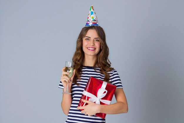 Mujer atractiva joven en gorra de celebración con regalo rojo y bebiendo una copa de champán