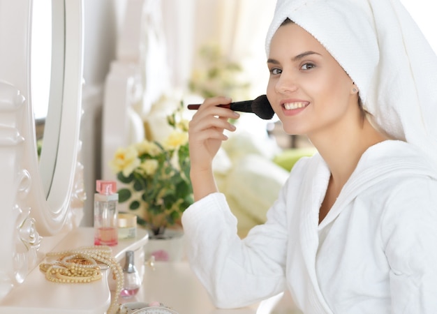 Mujer atractiva joven haciendo maquillaje después de la ducha en el tocador