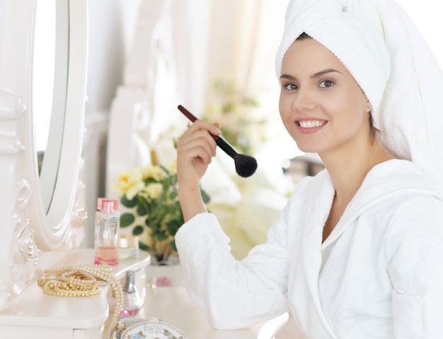 Mujer atractiva joven haciendo maquillaje después de la ducha en el tocador