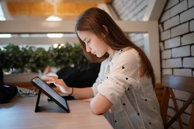 Mujer atractiva joven interactuando con la tableta móvil en el café