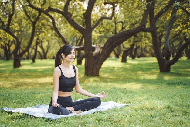 Foto mujer atractiva joven meditando en posición de loto sentado en el césped en el parque.