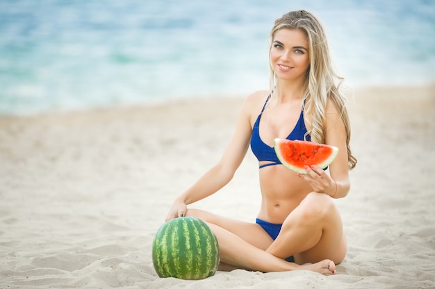 Mujer atractiva joven en la playa relajante. Mujer bonita con sandía. Linda chica al aire libre