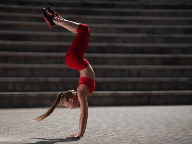 Mujer atractiva joven practicando yoga al aire libre. La niña realiza una parada de manos boca abajo