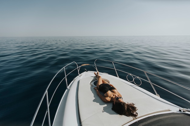 Mujer atractiva joven que se relaja en el yate de lujo que flota en el mar azul