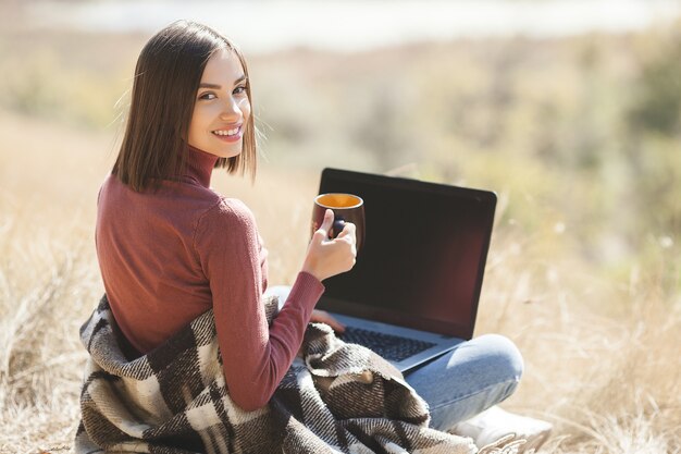 Mujer atractiva joven que trabaja en la computadora portátil al aire libre. Mujer haciendo su trabajo independiente en la pc. Trabajador remoto de vacaciones.