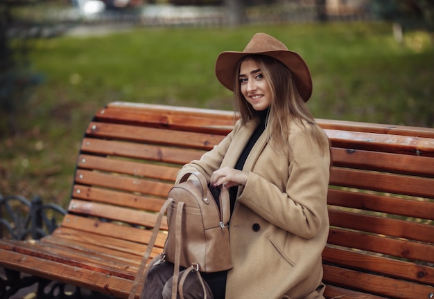 Mujer atractiva joven en ropa de otoño se sienta en un banco en el parque de la ciudad.