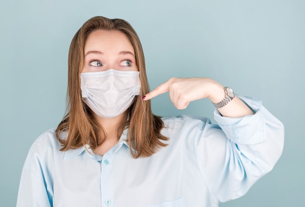 Mujer atractiva joven señala con el dedo una máscara protectora médica en su rostro. Prevención de la infección por coronavirus y resfriados.