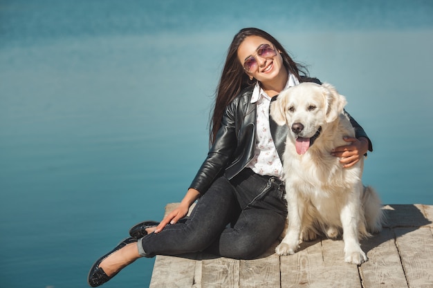 Mujer atractiva joven sentada en el muelle con su perro. Mejores amigos al aire libre