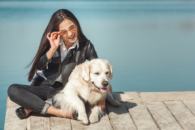 Mujer atractiva joven sentada en el muelle con su perro. Mejores amigos al aire libre