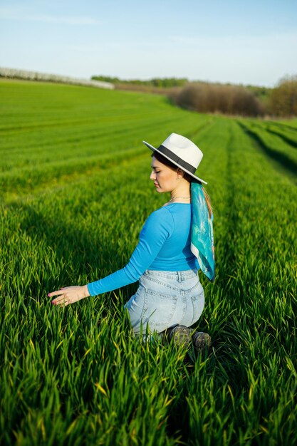 Mujer atractiva joven en sombrero blanco camisa azul jeans posando en campo verde de verano Copiar espacio vacío para texto