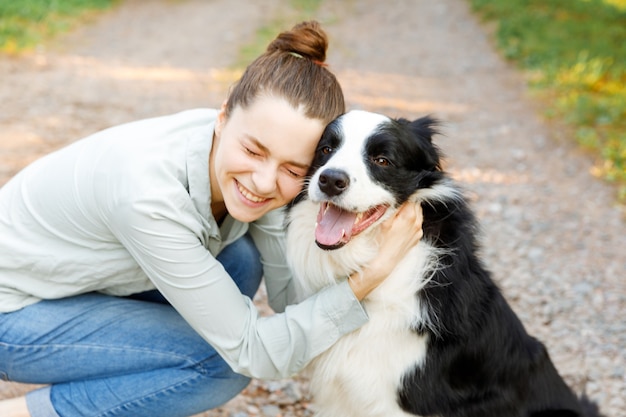 Mujer atractiva joven sonriente que juega con el border collie lindo del perrito del perro en el fondo al aire libre del verano. Chica sosteniendo abrazando abrazando a un amigo perro. Concepto de cuidado de mascotas y animales.