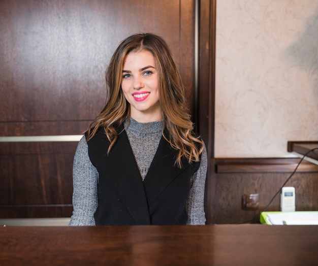 Foto mujer atractiva joven sonriente que se sienta en el escritorio en el hotel