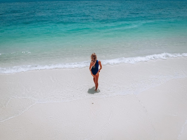 Mujer atractiva joven en un traje de baño azul de pie en una playa de arena y tomar el sol. Concepto de vacaciones de verano