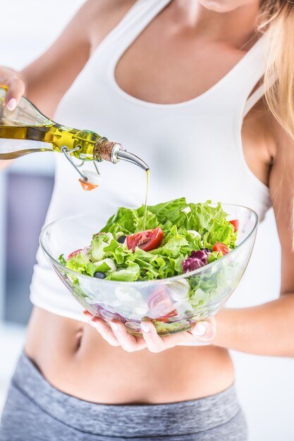 Mujer atractiva joven vertiendo aceite de oliva en la ensalada de verduras frescas.