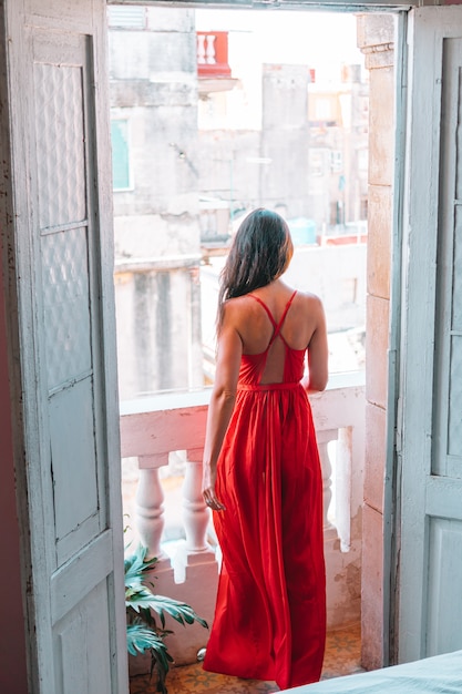 Mujer atractiva joven en vestido rojo en el balcón viejo en el apartamento en La Habana