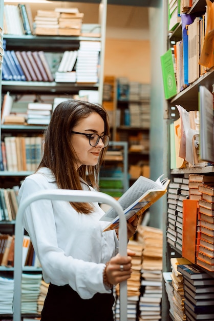 Mujer atractiva lee un libro mientras está de pie en la biblioteca