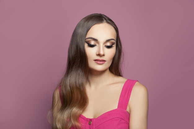 Mujer atractiva con maquillaje y cabello largo oscuro y saludable sobre un fondo rosa