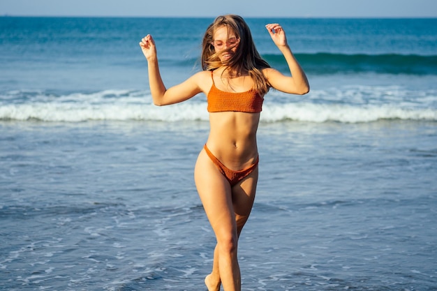Mujer atractiva pasando un buen rato en la playa. Chica joven belleza vistiendo la parte inferior del bikini traje de baño de color naranja coral con un cabello hermoso en el hermoso mar, el cielo y la isla tropical background.spf protector solar