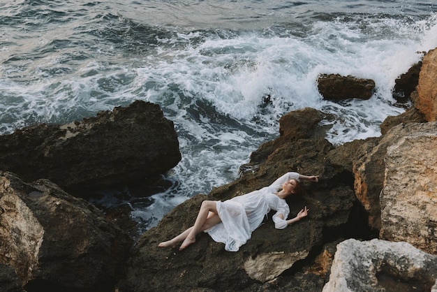Mujer atractiva con el pelo largo tumbado en la costa rocosa con grietas en el concepto de vacaciones de superficie rocosa