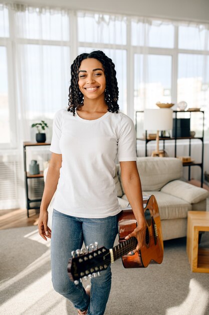 Mujer atractiva con poses de guitarra en casa. Señora bonita con instrumento musical relajarse en la habitación, amante de la música femenina descansando