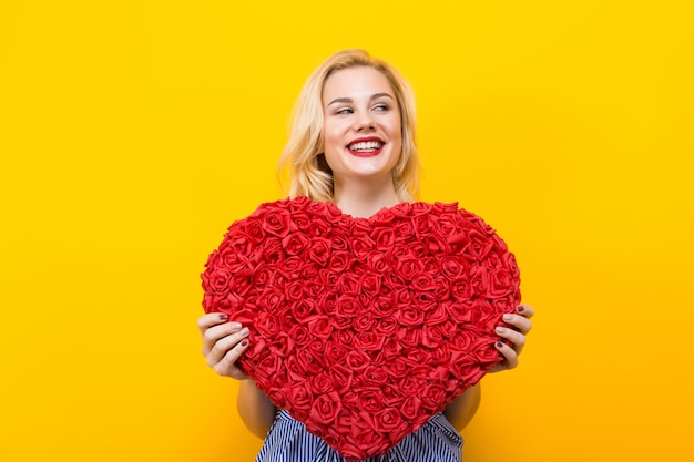 Mujer atractiva que lleva a cabo el corazón grande de la flor roja