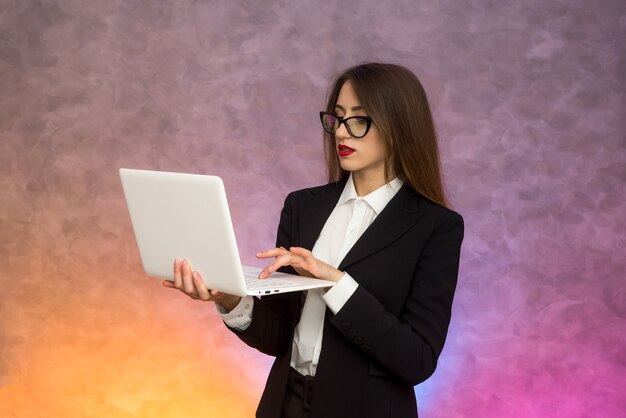 Mujer atractiva que sostiene la computadora portátil blanca. Secretario o estudiante o profesor posando sobre fondo abstracto