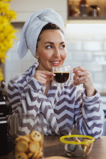 Una mujer atractiva relajándose y bebiendo café por la mañana en la cocina de casa.