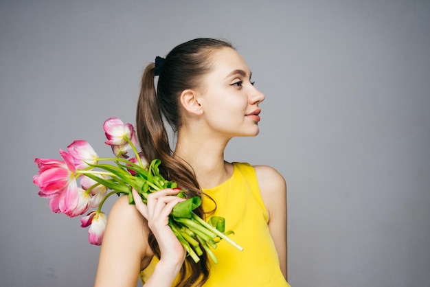 Mujer atractiva segura en vestido amarillo tiene ramo de flores y poses