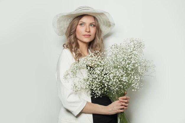 Mujer atractiva con sombrero de verano sosteniendo flores sobre un fondo blanco